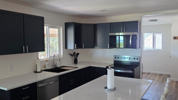 A modern kitchen with dark cabinets, a central island, and a dining area with chairs.
