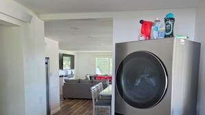 A modern kitchen with a built-in washer and dryer, a dining area with a table and chairs, and a view of the living room.