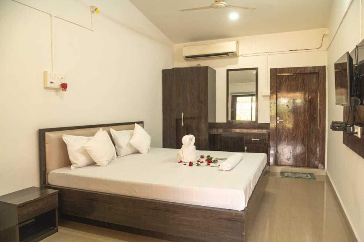 A bedroom with a bed, a wardrobe, a mirror, an air conditioning unit, and a television.
