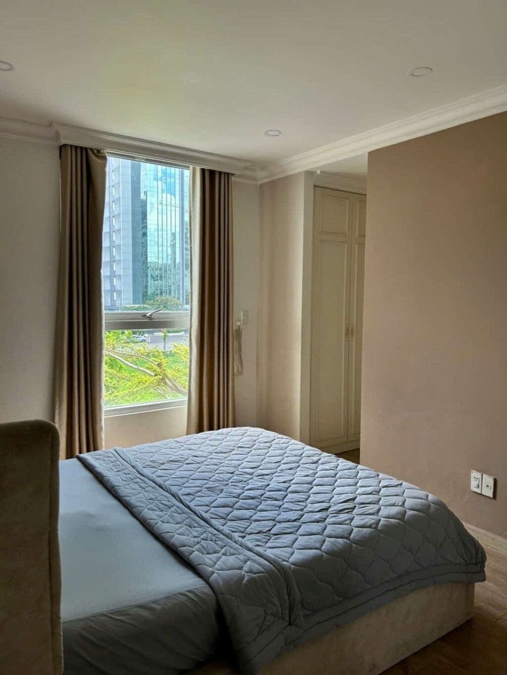 Une chambre à coucher avec un lit, une chaise, une fenêtre avec des rideaux et une vue sur les bâtiments à l’extérieur.