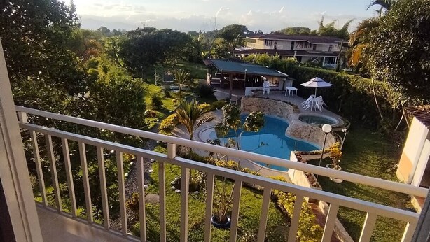 A balcony with a view of a swimming pool, a covered patio, and surrounding greenery. - El Amanecer Farm Hotel (Quimbaya)