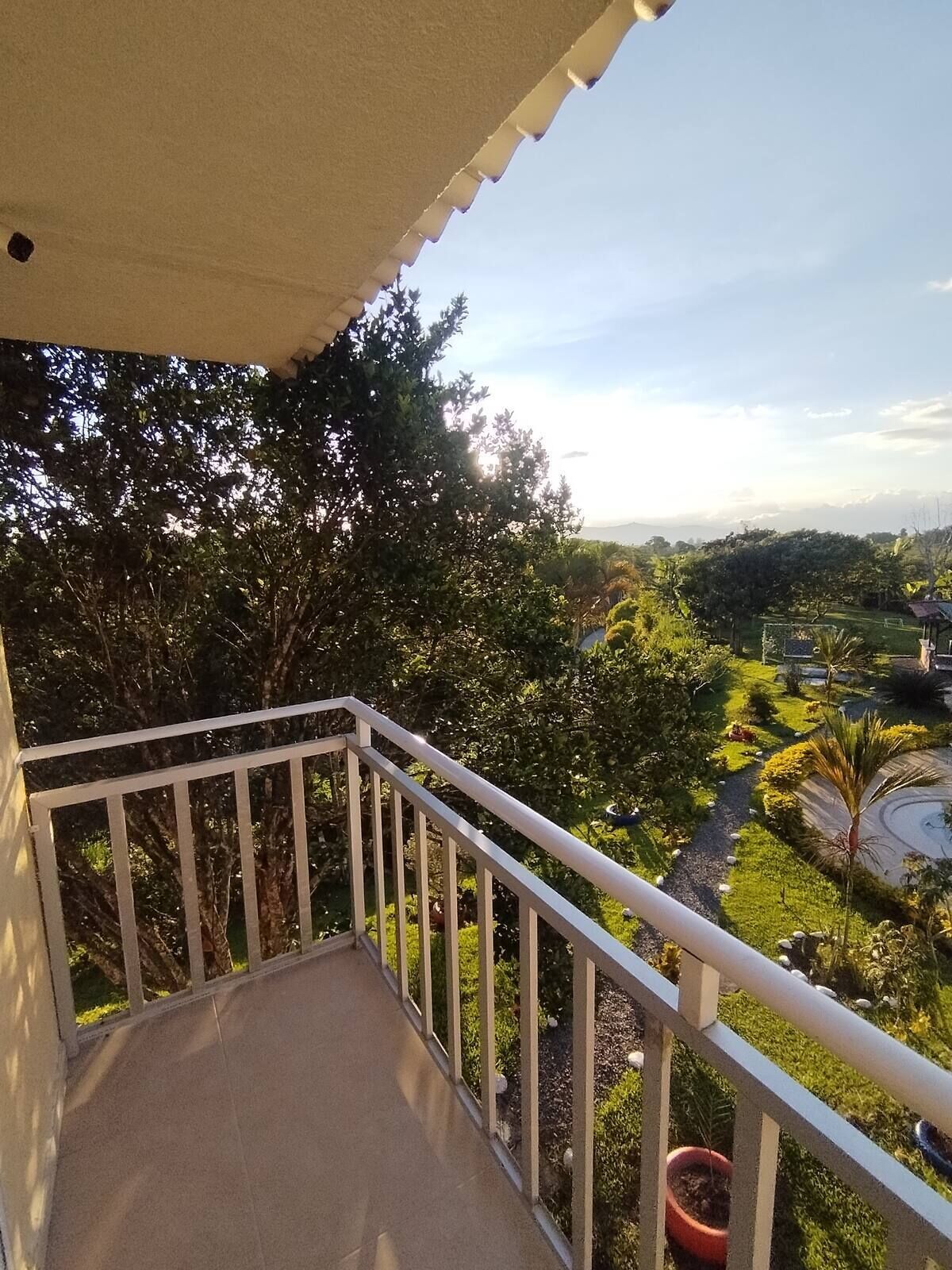 Un balcon donnant sur un jardin aménagé et sur des collines lointaines.