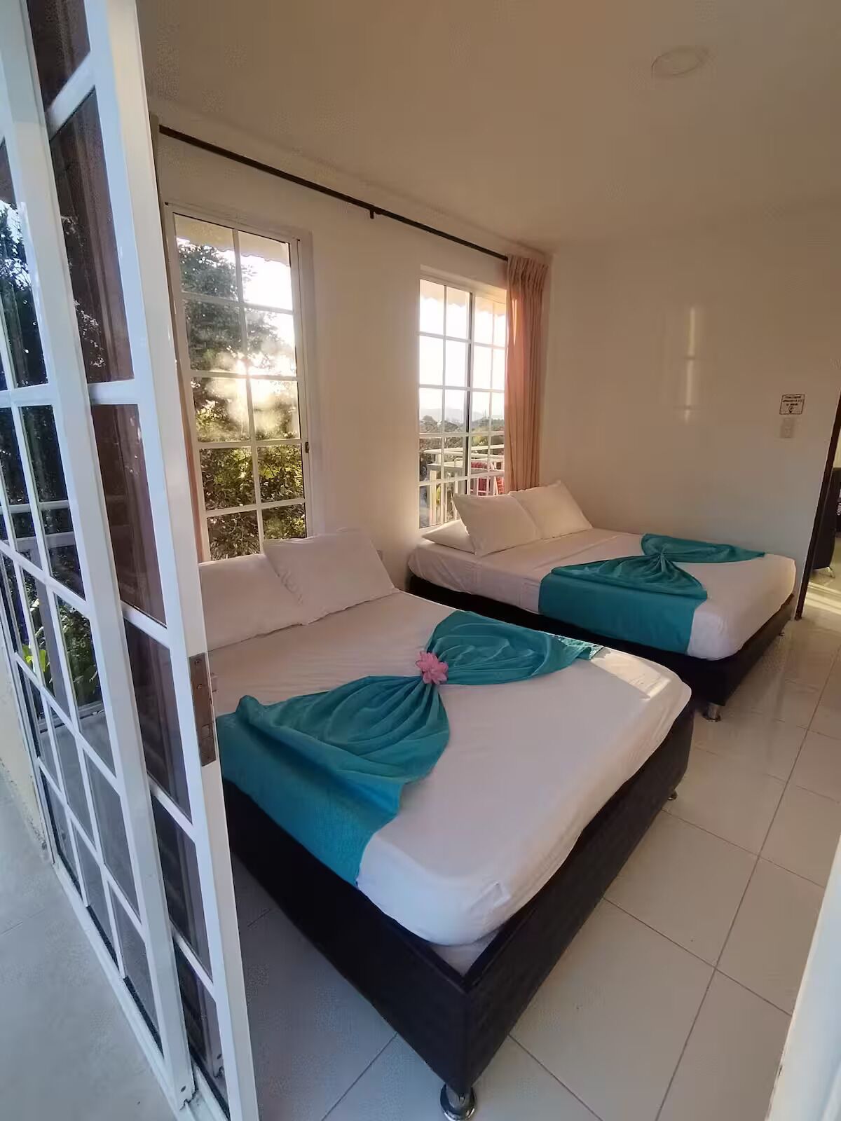 A hotel room with two beds, a sliding glass door, and a view of the outdoors.