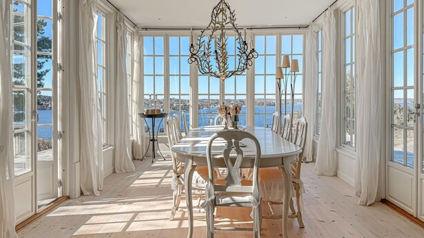 A sunlit dining room with a view of the sea, a chandelier, and a table set for six. - Lovely home in Saltsjöbaden with sauna (Saltsjöbaden)