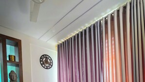 Ein Wohnzimmer mit einem beigefarbenen Ecksofa, einem Deckenventilator, einer Buddha-Statue und einer Wanduhr.