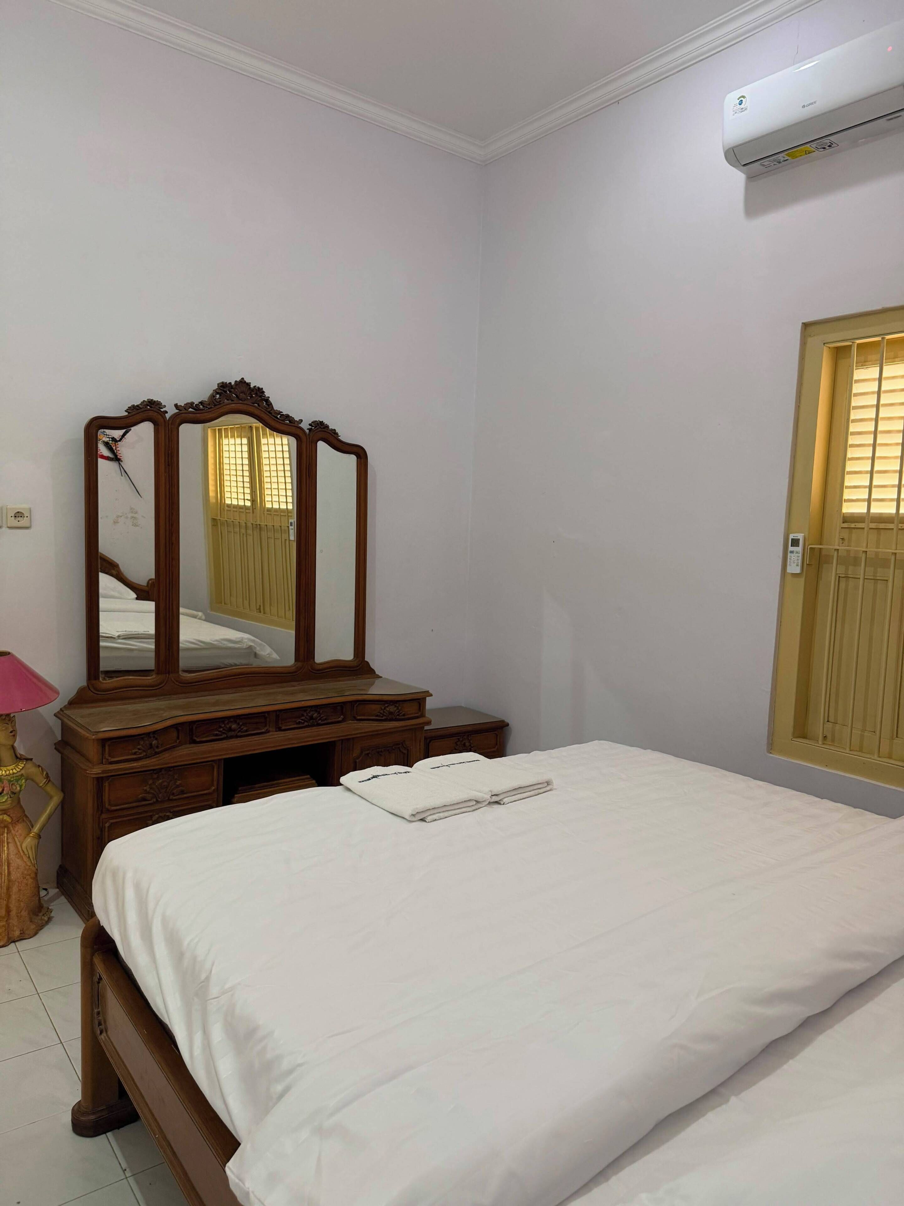 A bedroom with a bed, a wooden dresser, a mirror, and an air conditioning unit.