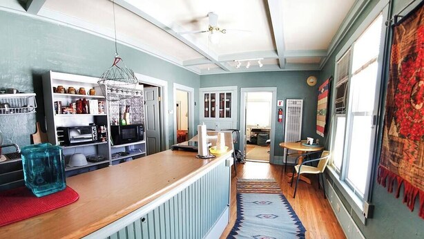 A kitchen with a wooden countertop, a hanging light fixture, and a view into the dining area. - The Mini Place, Buffalo (Buffalo)