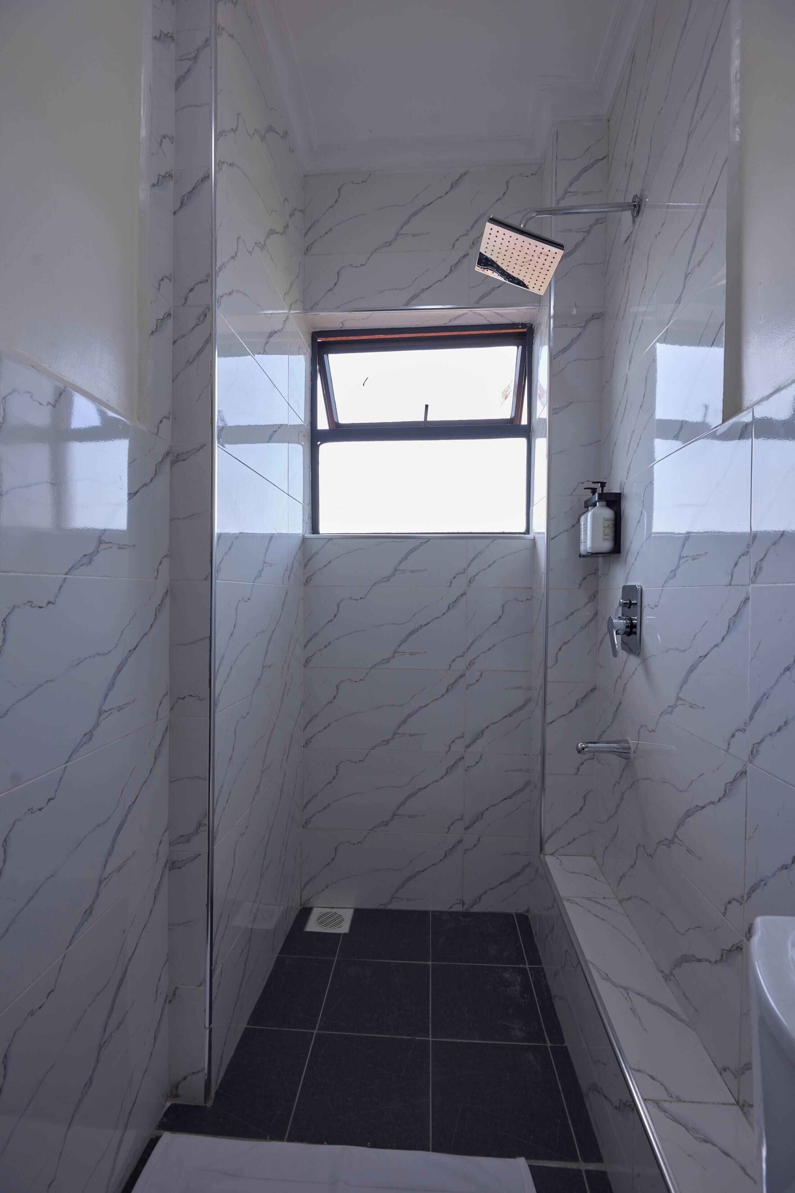 A shower with a glass door, a window, and a tiled floor.