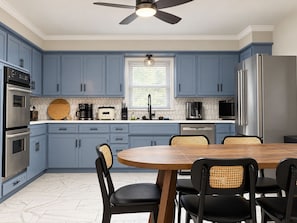 A modern kitchen with blue cabinets, a wooden dining table, and black chairs. - Minutes to Arrowhead! 4BR Home with pool table, finished basement & Fire Pit (Kansas City)