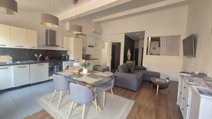 A modern kitchen with a dining area, a grey sofa, and a TV mounted on the wall. - In the heart of the harbor with a rooftop view of the ocean (La Ciotat)