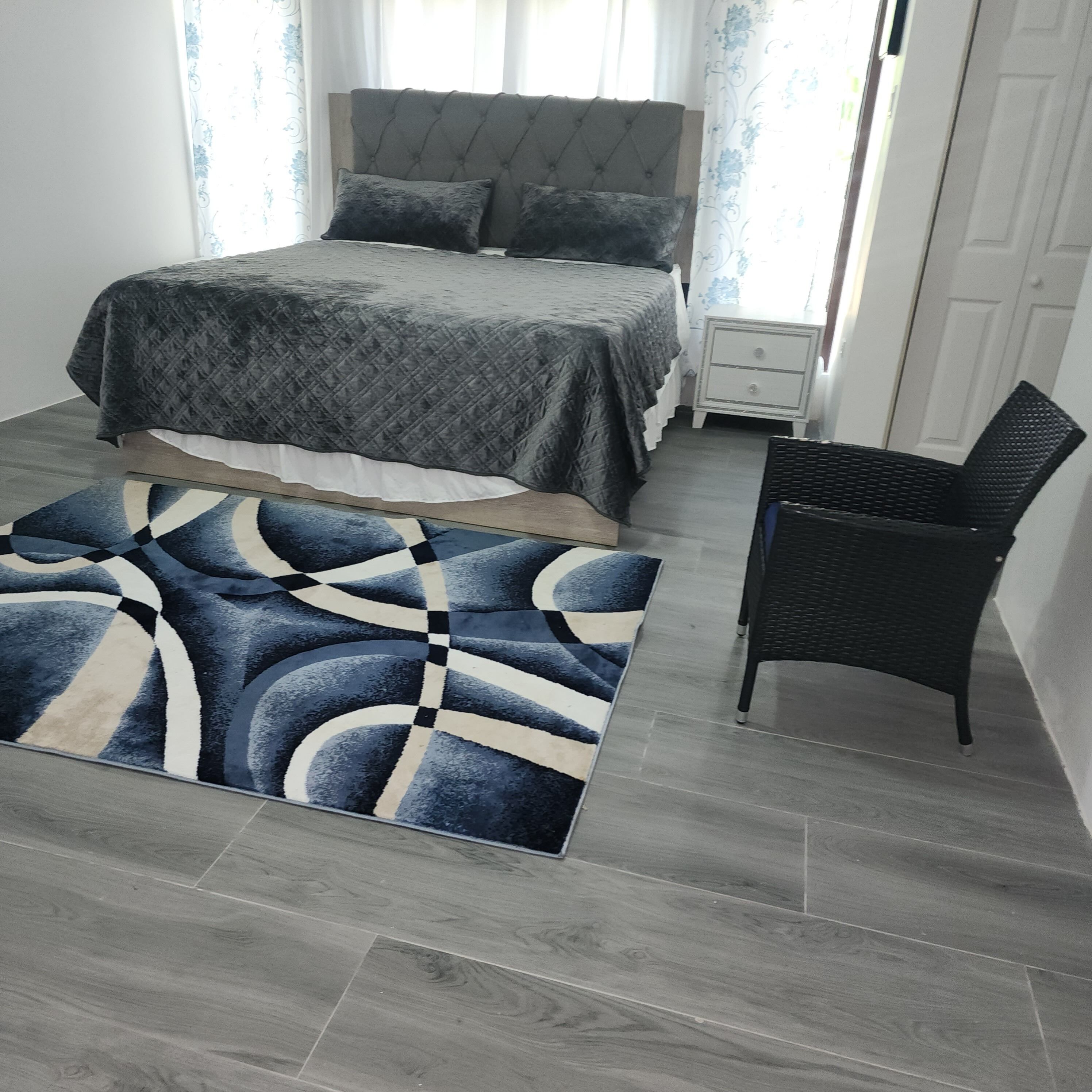 A bedroom with a bed, a nightstand, a chair, and a patterned rug.