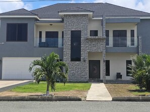 A two-story residential building with a garage, a stone accent wall, and a small front yard with palm trees. - Ocean view oasis 3bedrooms (Portland)