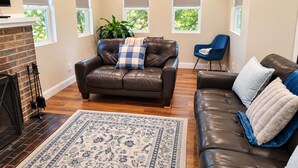 Uma sala de estar com um sofá de couro marrom, uma poltrona azul e um tapete estampado.