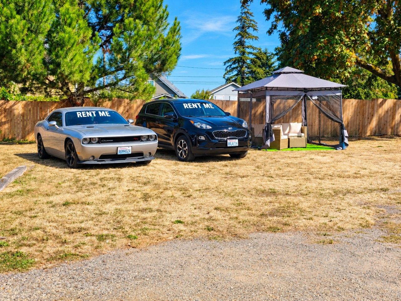 Two cars parked in a yard with a tent and a wooden fence in the background.