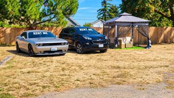 Two cars parked in a yard with a tent and a wooden fence in the background.