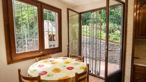 A dining area with a table and chairs, a window with a metal grill, and a door leading to an outdoor garden.