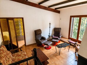 Quarto com sofá, duas poltronas, uma mesinha, um banco e janela com vista para o verde.