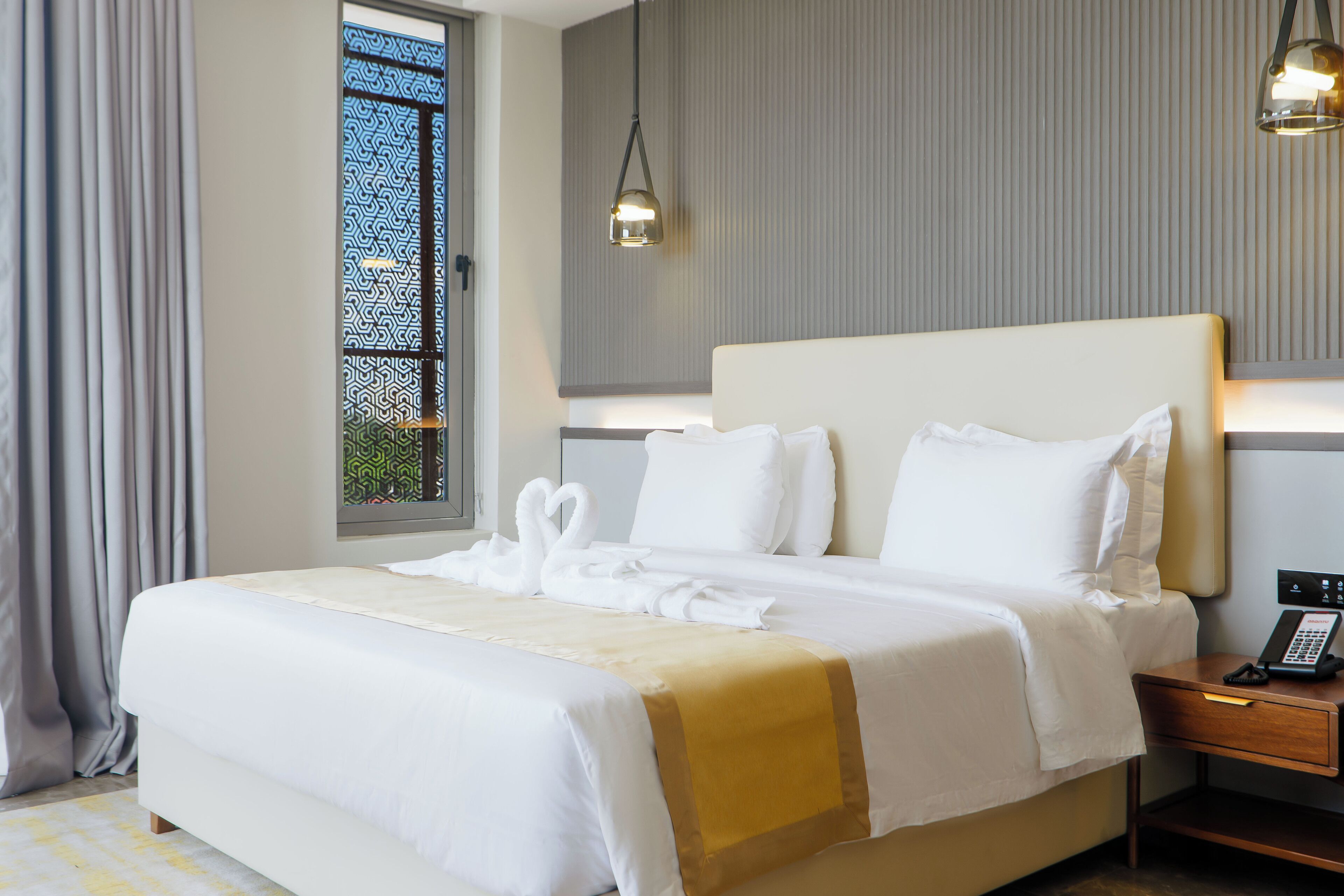 Een hotelkamer met een groot bed, een nachtkastje met telefoon en een raam met uitzicht.