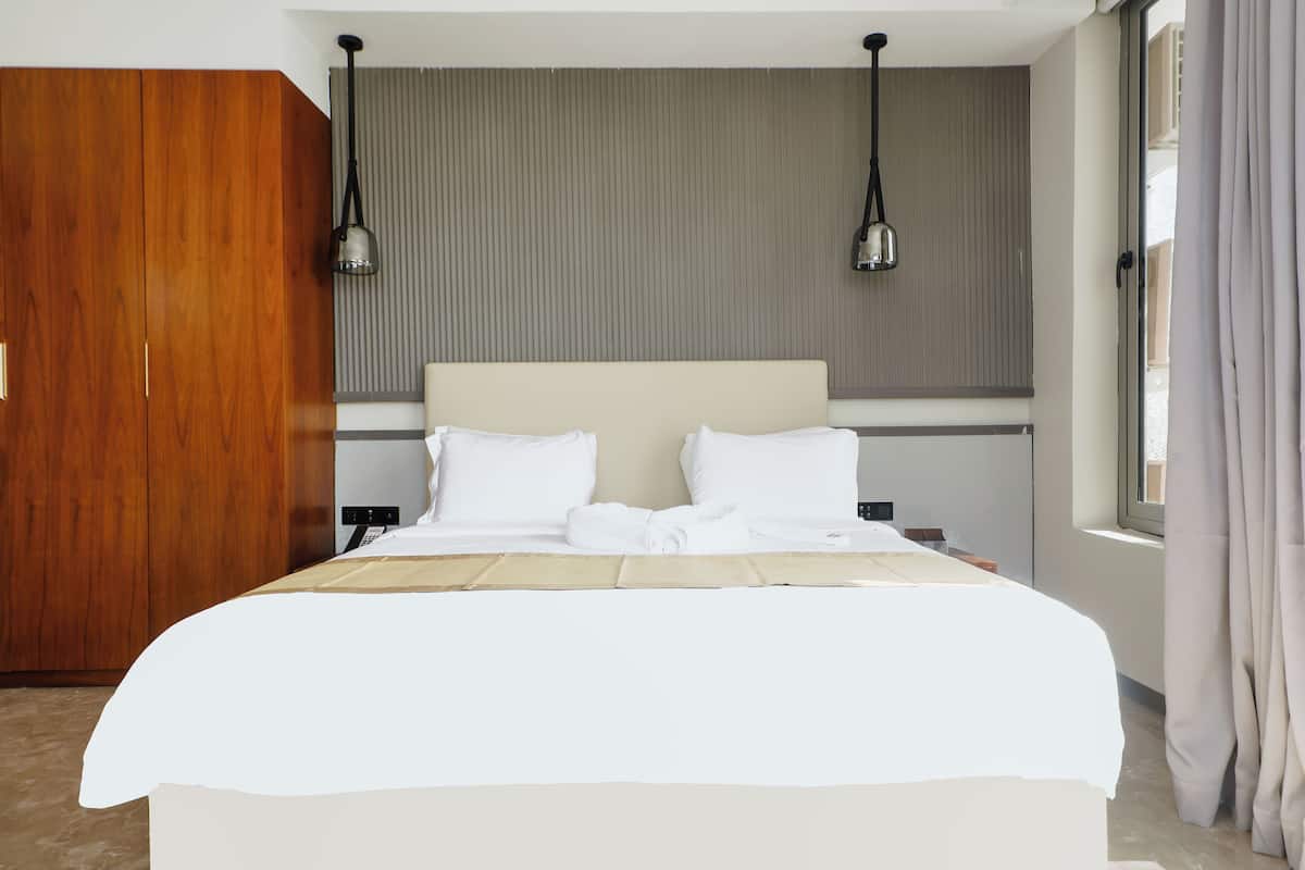 Una habitación de hotel con una cama grande, un armario de madera y dos lámparas colgantes.
