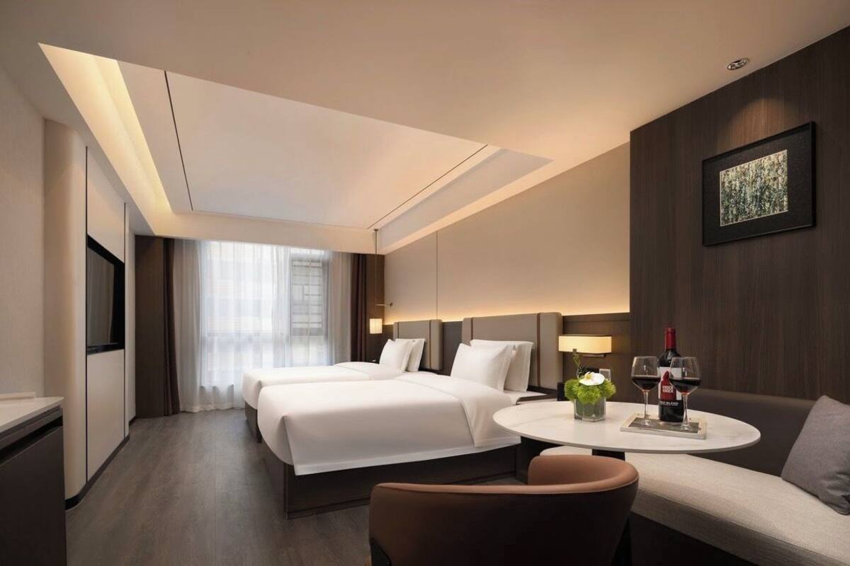 Habitación de hotel con dos camas, un sofá, una mesita con copas de vino y un televisor.