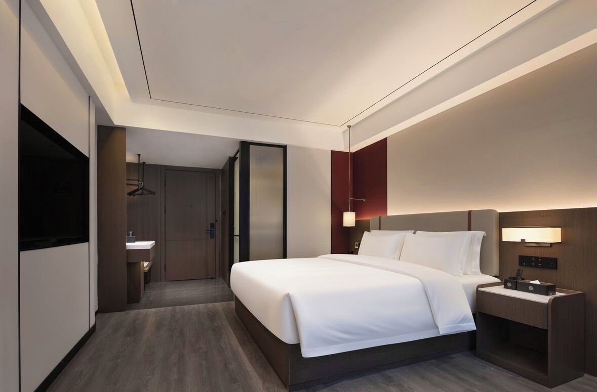 Una habitación de hotel moderna con una cama grande, mesitas de noche, un televisor y un baño.