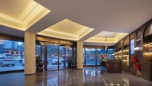 A hotel lobby with a glass entrance, a reception desk, and a view of the street outside.