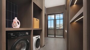 A laundry room with a washer and dryer, a wooden cabinet with a bottle, and a view through a glass door.