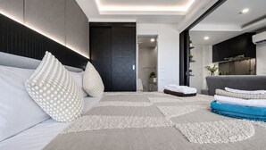 A modern living room with a sofa, patterned cushions, a rug, and a kitchen area visible through an open door. - Aristo 1BR Coastal Escape in Surin Beach (Tambon Choeng Thale)