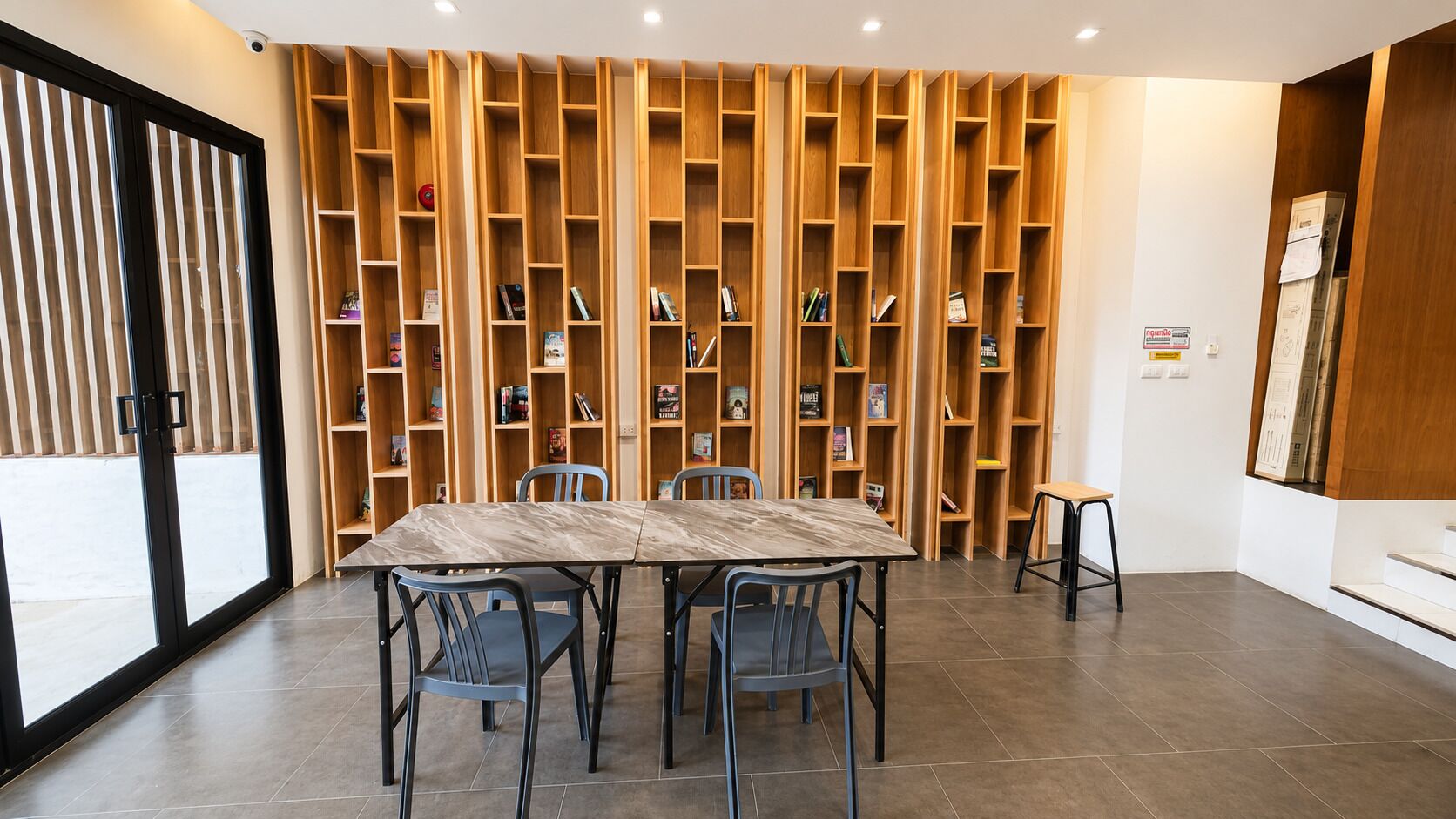 A room with a marble-tiled floor, a wooden bookshelf wall, a table with chairs, and a small stool.