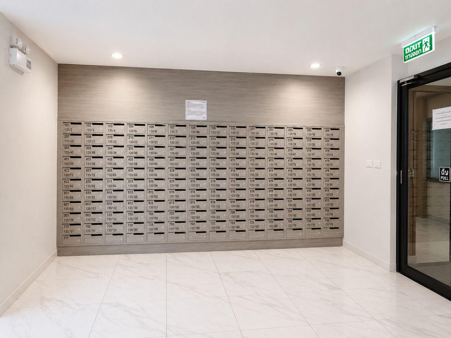 Eine Reihe von Hotelzimmern mit nummerierten Türen, ein Schild, das einen Ausgang kennzeichnet, und ein sauber gefliester Boden.