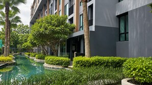A modern hotel with a swimming pool, lush greenery, and a multi-story building with large windows. - Aristo 1BR Coastal Escape in Surin Beach (Tambon Choeng Thale)