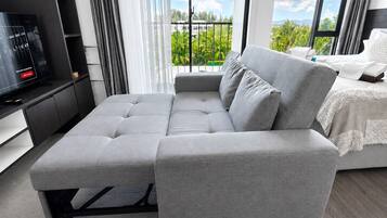 Un moderno salón con un sofá seccional gris, un televisor de pantalla plana y un balcón con vistas a zonas verdes y edificios.