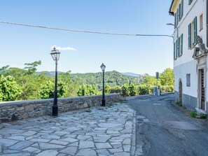 A stone-paved pathway leading to a building with a stone wall and two street lamps. - Queen Bee by Interhome (Ponzone)