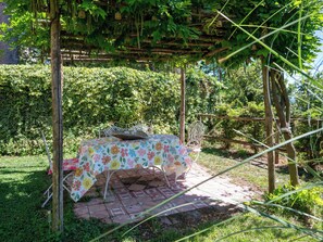 A garden setting with a table under a pergola, surrounded by greenery. - Queen Bee by Interhome (Ponzone)