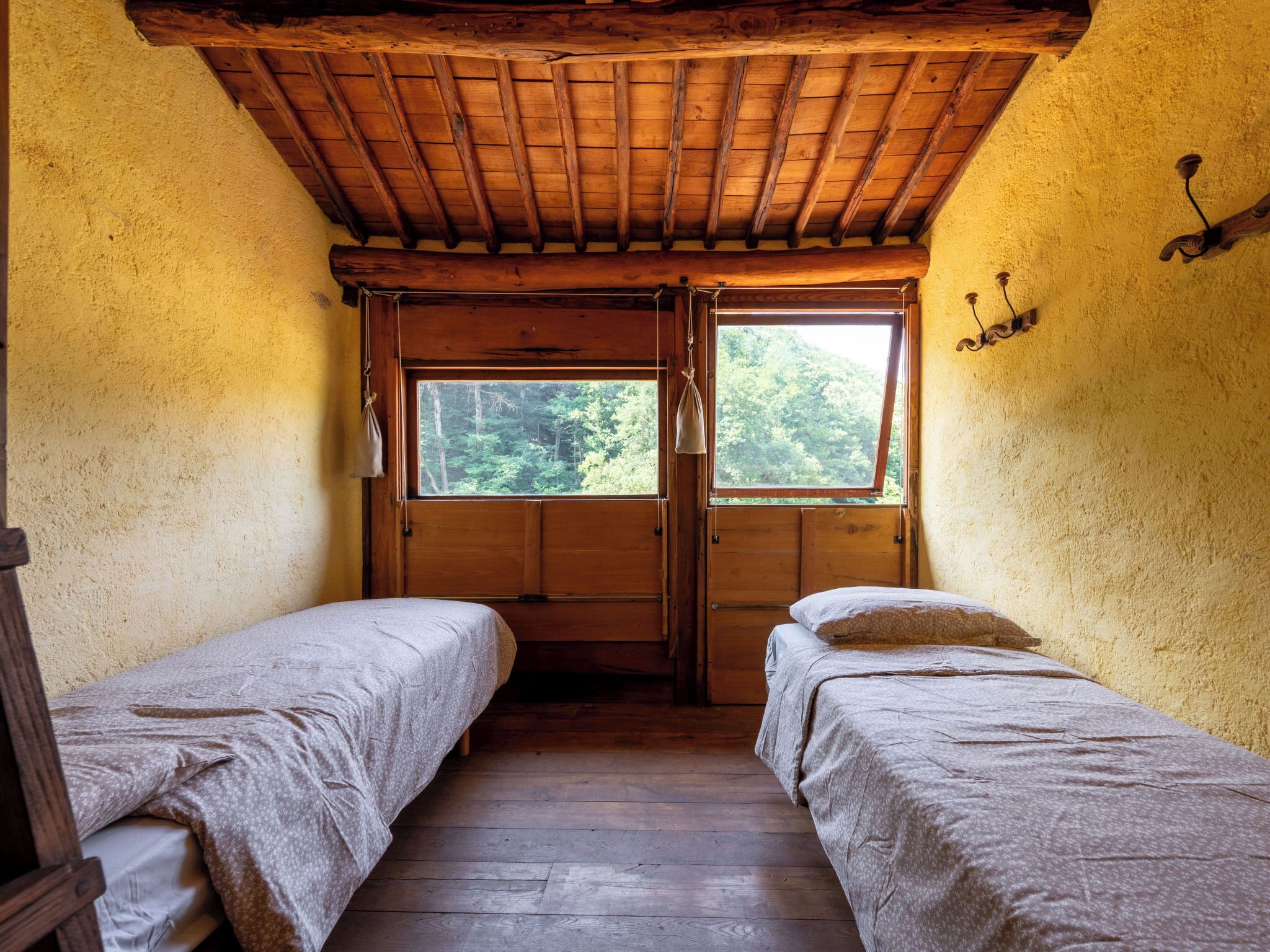 Una cabaña con dos camas individuales, vigas de madera en el techo, un ventanal con vistas a árboles y un interior rústico.