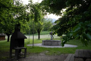 Ein Park mit einem Grill, einem Steinkrugbrunnen und Picknicktischen.
