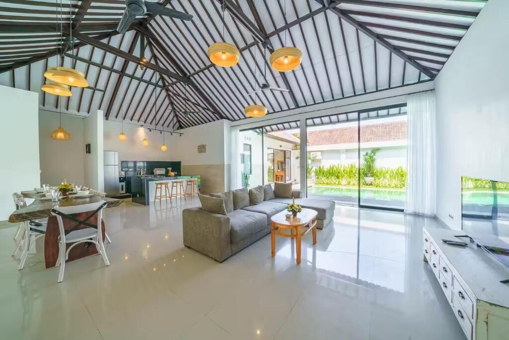 A spacious living area with a high ceiling, a sofa, a dining table, and a kitchen in the background.