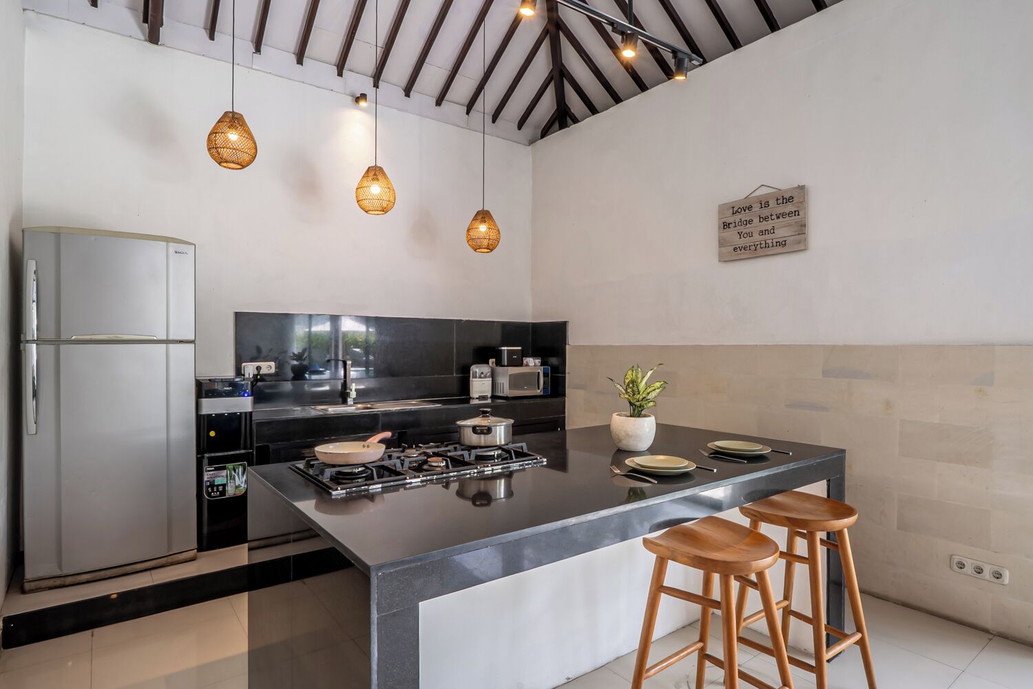 Una cocina moderna con una isla central, electrodomésticos de acero inoxidable, iluminación colgante y un letrero decorativo.