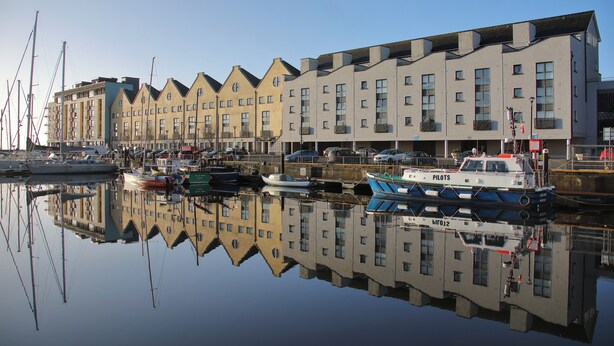 A waterfront building with multiple balconies and a reflection in the water.