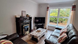 A living room with a fireplace, a television, a sofa set, and a window with curtains.