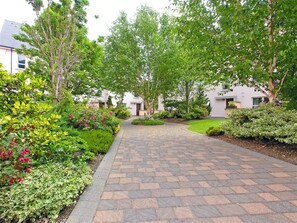 A paved pathway leading to a building with a modern architectural style, surrounded by lush greenery and flowering plants. - Galway Dockside Townhouse (Galway)