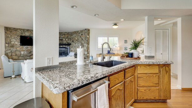 A kitchen with a granite countertop, wooden cabinets, a stone wall, and a built-in dishwasher. - Golf Course Retreat: Pool, RV/Boat Pkg, Lake Views (Lake Havasu City)