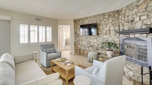 A living room with a stone wall, a flat-screen TV, a sofa, a chair, a coffee table, and a small round table. - Golf Course Retreat: Pool, RV/Boat Pkg, Lake Views (Lake Havasu City)