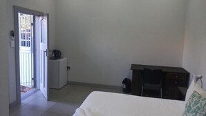 A hotel room with a bed, a desk, a chair, a small cabinet, and a door leading to a balcony. - Triple9 Guesthouse (Hatfield, Pretoria)