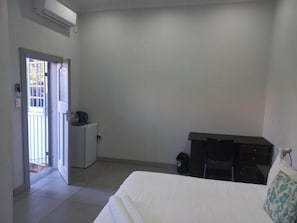 A hotel room with a bed, a desk, a chair, a small cabinet, and a door leading to a balcony.
