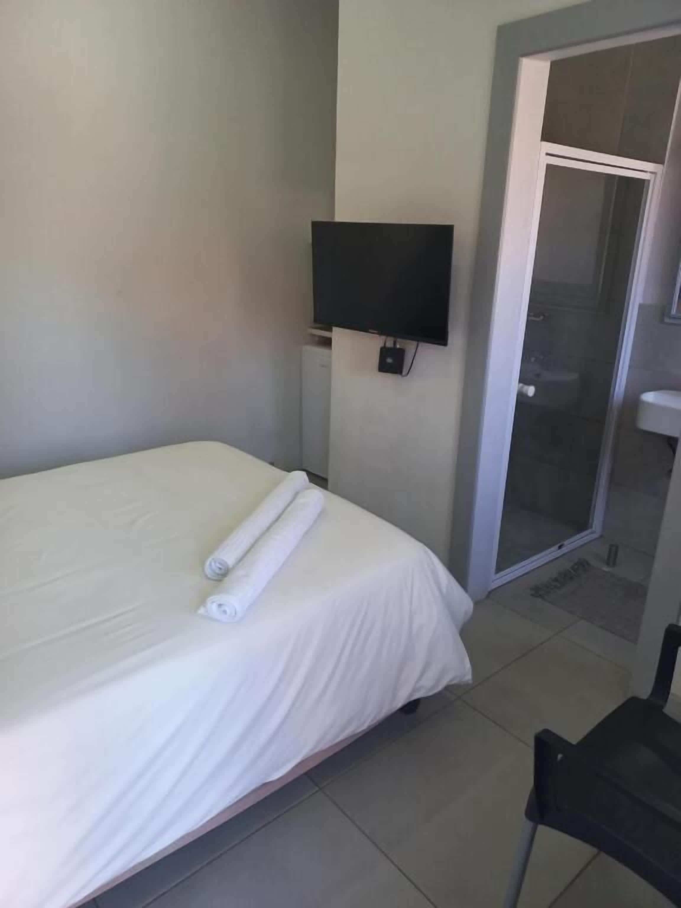 A hotel room with a bed, a TV mounted on the wall, and a sliding glass door leading to a bathroom.