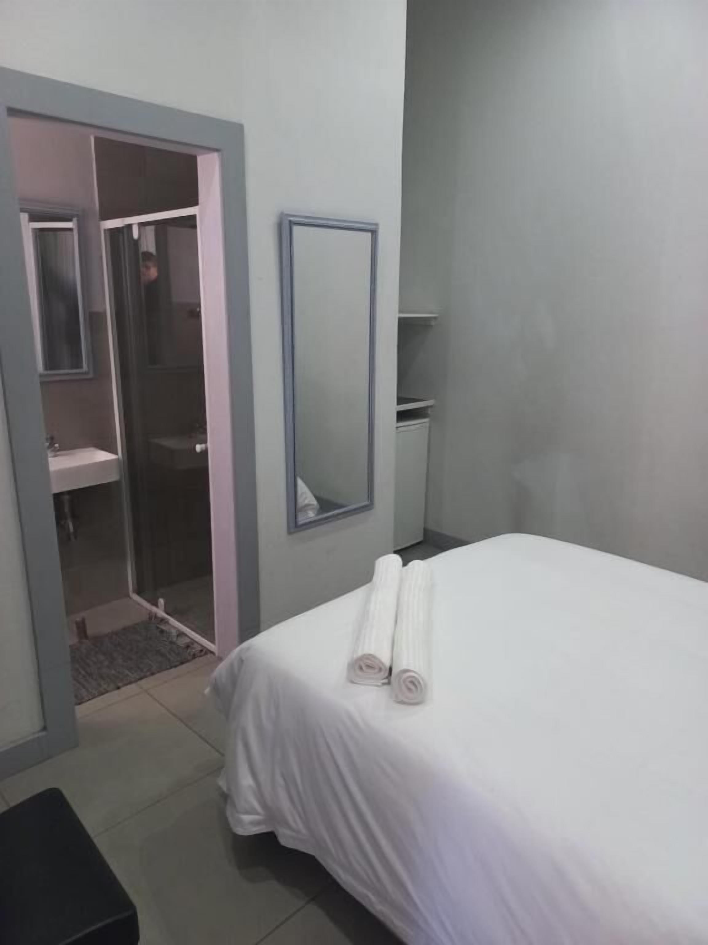 Une chambre d’hôtel avec un lit, un miroir, une douche et une petite table.