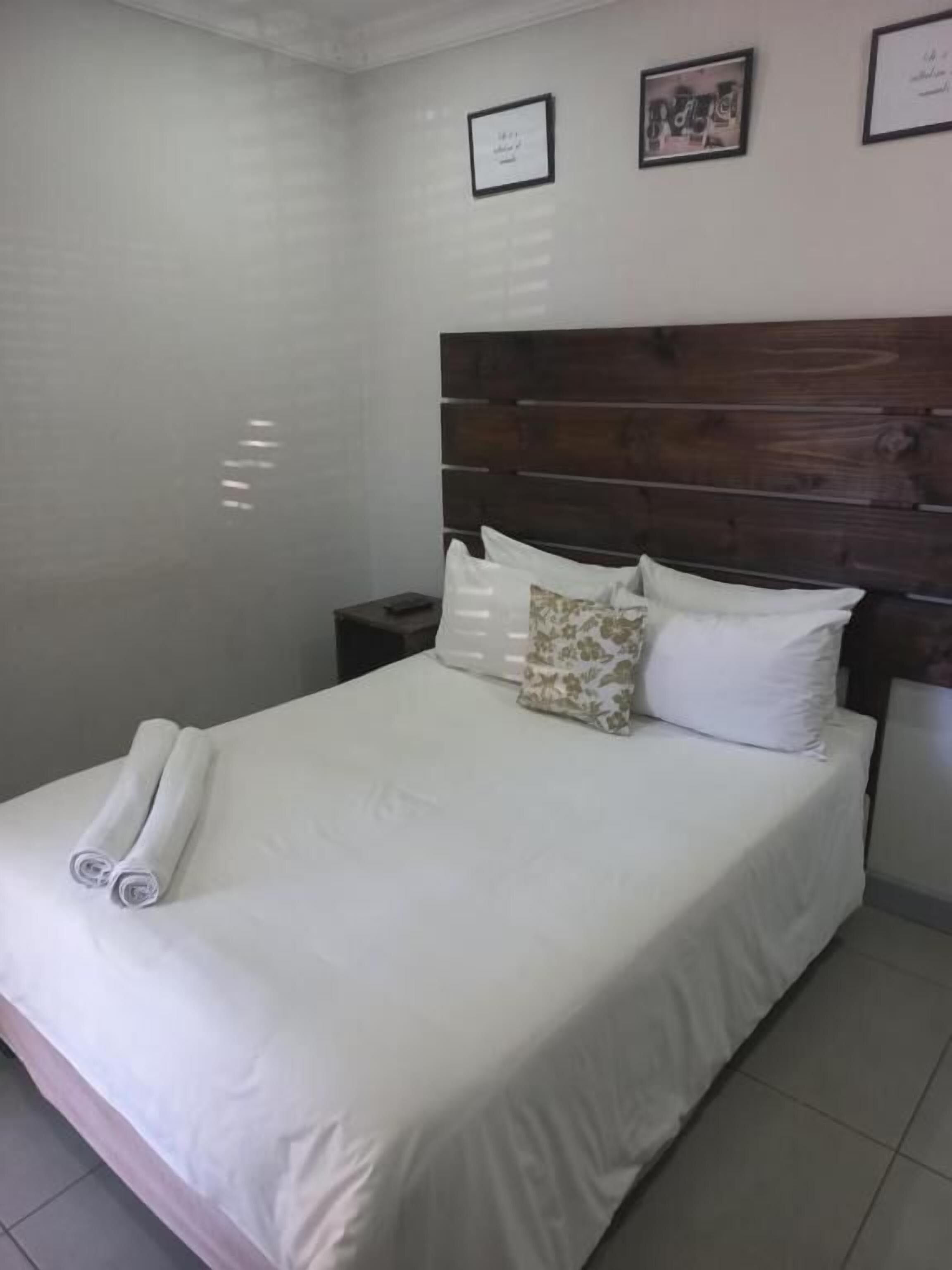 Una cama bien hecha con sábanas blancas y un cabecero de madera, una mesita de noche con una lámpara y un cuadro en la pared.
