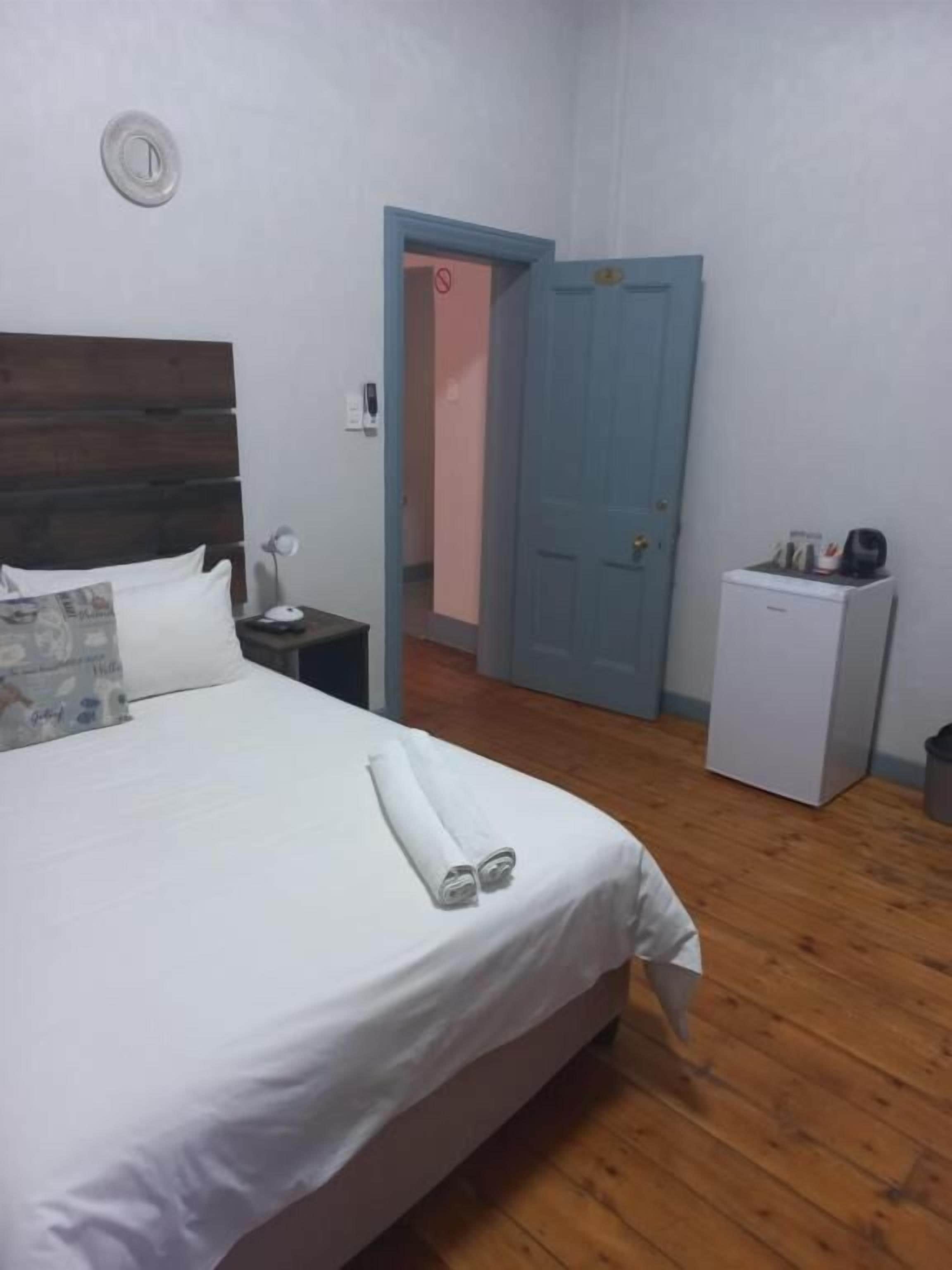 Un dormitorio con una cama, un mesita de noche, un refrigerador blanco pequeño y una puerta azul.