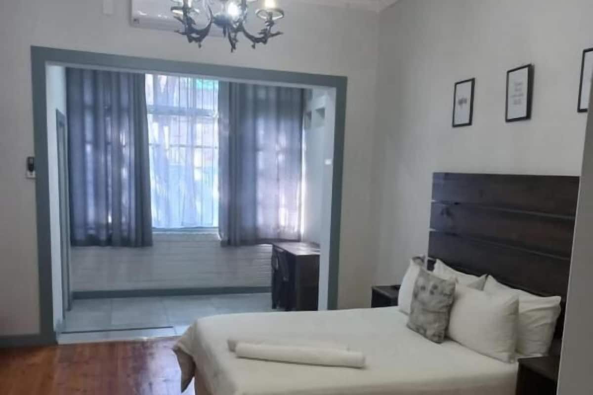 A bedroom with a large bed, a chandelier, a wooden floor, and a view through a glass door.